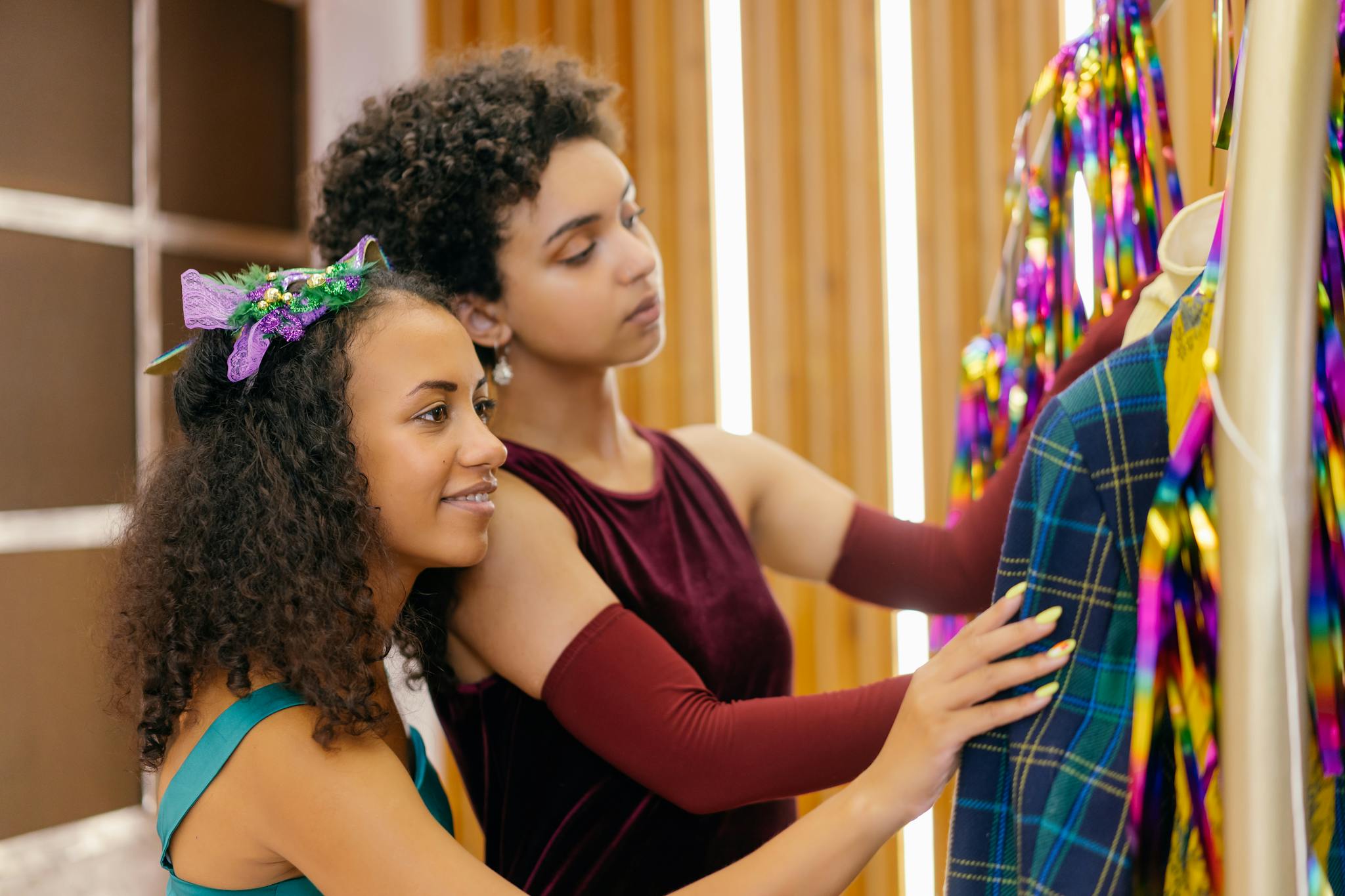 Two young women explore colorful dresses in vibrant indoor setting.